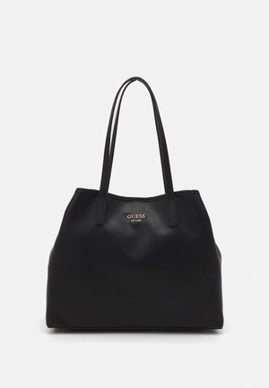 Sort læder tote-taske med to lange håndtag og gyldent "GUESS EST 1981" logo centreret nær toppen foran.