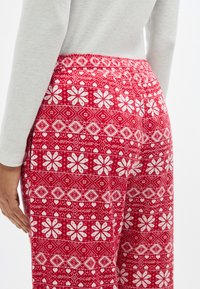 Pantalon de pyjama rouge à motifs avec des designs floraux blancs et géométriques. Tissu doux avec une taille élastique, vu de dos.
