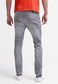 Šedé džínové kalhoty s úzkým střihem, mají dvě zadní kapsy a jemné prošívací detaily. Kombinované s bílými teniskami a oranžovým topem.