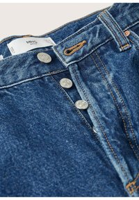 Vaqueros de denim con cierre de botón y botones plateados, tono azul claro y detalles de costura visibles. La etiqueta muestra la información de la marca y de cuidado.