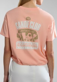 Růžové bavlněné tričko s krátkým rukávem a zkráceným spodním lemem, s předním a zadním grafickým potiskem "CANOE CLUB" a scénickými prvky.