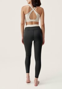 Beige sport-beha met X-back ontwerp en uitsnijding, gecombineerd met slim-fit zwarte leggings, beide gemaakt van rekbare, vochtdoorlatende stof.