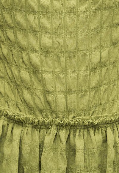 Ανοιχτοπράσινο ύφασμα με υφή ελαστικού σμόκινγκ και λεπτομέρεια ραφής με βολάν κοντά στην κάτω άκρη.