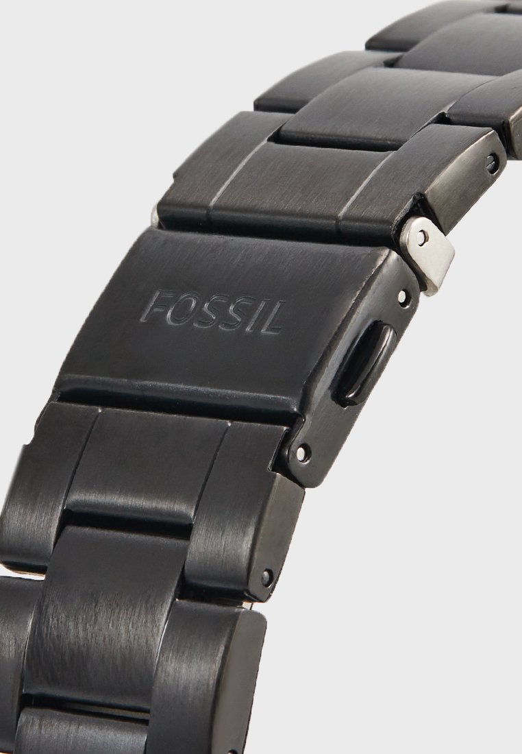 Cinturino per orologio in metallo nero con texture spazzolata, dotato di maglie intrecciate e una fibbia; logo "FOSSIL" incisa su una maglia.