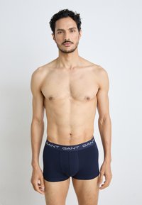 Boxers en coton bleu marine avec une ceinture de logo blanche contrastée. Le tissu semble lisse, avec un design ajusté et sans motifs visibles.