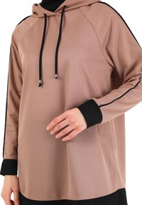 Camiseta con capucha de manga larga en rosa claro con detalles en negro. Presenta un tejido texturizado y cintas ajustables, con detalles en negro en los puños y el dobladillo.