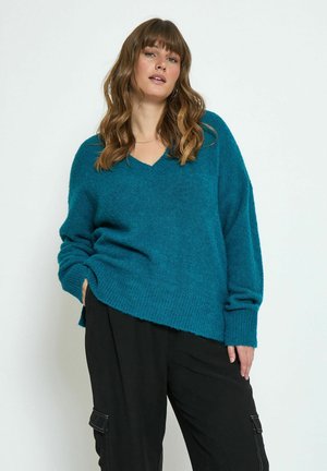 Teal, oversized knit sweater with a V-neck and ribbed hem. Soft texture, dropped shoulders, and long sleeves. Paired with black pants.