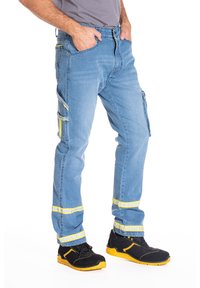 Pantalons cargo en denim bleu avec des accents réfléchissants jaunes, design à jambe droite, plusieurs poches et poignets contrastés. Portés avec des chaussures noires.