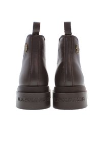 Botas de cuero marrón hasta el tobillo con una suela gruesa, lengüetas de tirón y un logotipo grabado en el talón. Detalle decorativo del logo en el lateral.