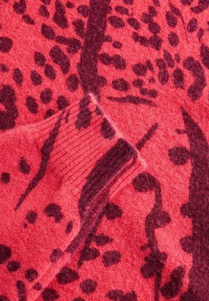 Tissu rouge texturé avec des taches léopard abstraites de couleur bordeaux foncé, présentant des accents côtelés et un aspect tricoté mélangé.