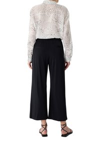 Czarne spodnie o szerokich nogawkach z elastycznym paskiem w talii, zestawione z przezroczystą białą bluzką w kropki. Całość dopełniają czarne sandały na paski.