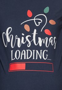 Sötétkék póló, fehér "Karácsony betöltése..." felirattal, színes izzó grafikákkal piros, zöld és barna színekben, valamint egy piros előrehaladási sávval.