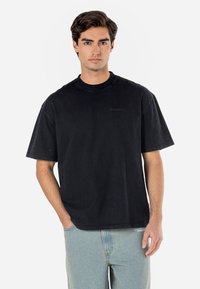 T-shirt noir oversize en coton, avec des manches courtes et un col rond. Détail logo subtil sur le devant. Coupe décontractée.