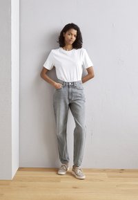 Lichtgrijze denim jeans met een hoge taille, gecombineerd met een wit T-shirt met korte mouwen en beige sneakers, tegen een minimalistische achtergrond.