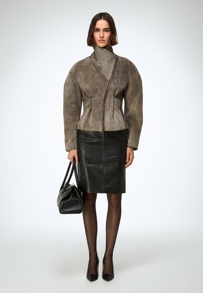 Szürke velúr dzseki aszimmetrikus cipzárral, magas gallérral és dús ujjakkal, összehangolva egy testhezálló fekete bőr szoknyával és fekete magassarkúval.