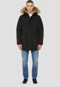 Sort parka-jakke med hætte i imiteret pels, lynlås foran, to forlommer og justerbare snore. Bær den over afslappede lyse jeans og sneakers.