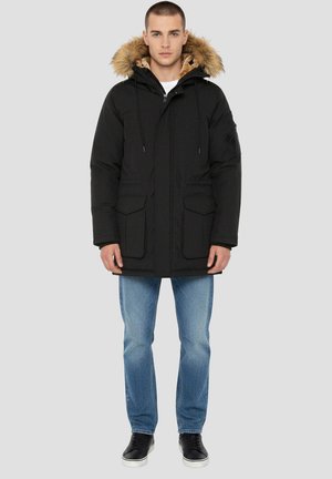 Sort parka-jakke med hætte i imiteret pels, lynlås foran, to forlommer og justerbare snore. Bær den over afslappede lyse jeans og sneakers.