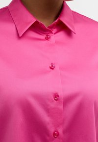 Bright pink shirt made with smooth fabric features a pointed collar and matching buttons down the front. No visible patterns or accents.