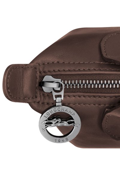 Brown leather bag zipper with silver round Longchamp 1948 logo charm featuring a horse and rider.