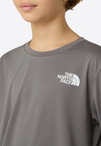 Sivá tričko s krátkym rukávom z hladkej tkaniny s bielym logom North Face na ľavej strane hrudníka. Okrúhly výstrih s voľným strihom.
