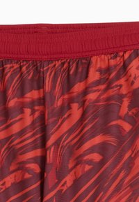 Pantaloni corti rossi con una cintura elastica, caratterizzati da un motivo grafico di pennellate rosso scuro e arancione su un tessuto texturizzato.