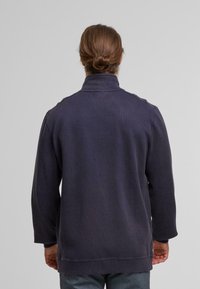 Fleecejacke in dunkelblau mit hohem Kragen, langen Ärmeln und lockerer Passform. Glatte Textur mit sichtbaren Nähten.