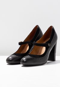 Zwarte leren pumps met een ronde neus, suède accenten, geperforeerde details en een blokhak, met een riempje over de wreef.