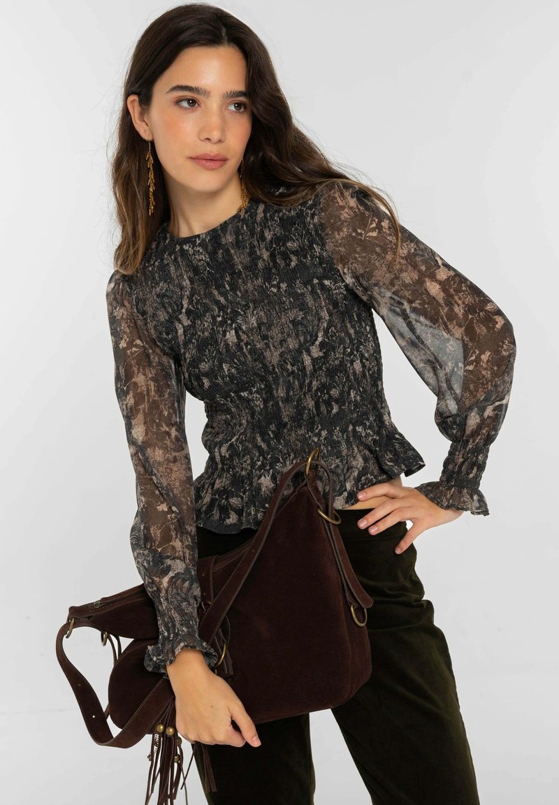 Blusa con estampado en negro y marrón, cintura fruncida y mangas largas transparentes, combinada con un bolso de hombro de ante marrón oscuro.