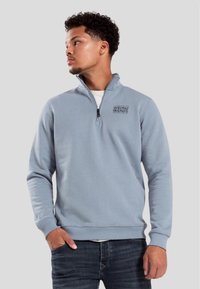 Ljusblå zip-up sweatshirt gjord av mjukt tyg. Har en hög krage och en logotyp "WRONG FRIENDS" tryckt på bröstet. Avslappnad passform.