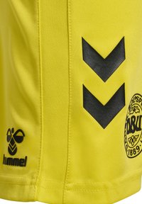 Gul sportströja i syntetmaterial, med svarta chevronmönster, en logotyp med ett runt emblem och strukturerad tygfinish.