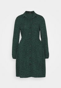 Vestito verde a maniche lunghe con bottoni, caratterizzato da un piccolo motivo floreale nero e colletto, vita aderente e gonna leggermente svasata.