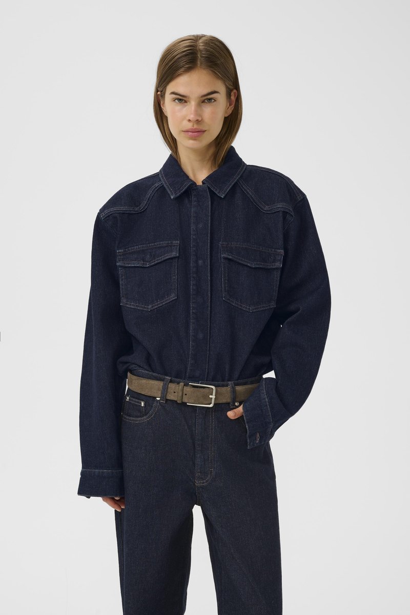 Chemise en denim foncé avec un col, deux poches poitrine et des manches longues. Associée à un pantalon en denim foncé taille haute et une ceinture kaki.