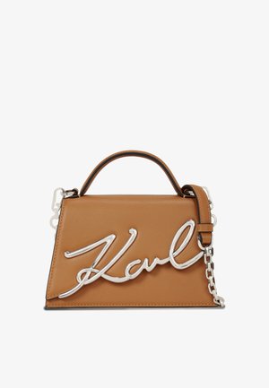 Brun skinnveske med sølvfargede detaljer. Har et topphåndtak og lang kjede-rem. Framsiden har en stilisert "Karl" signatur.