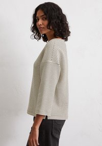 Striped, loose-fitting crew neck top in cream and black with three-quarter sleeves, featuring side slits and a textured knit fabric.
