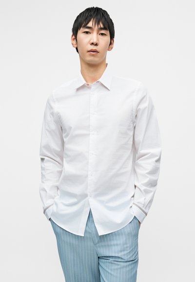 Λευκό πουκάμισο με κουμπιά, κλασικό γιακά, μακριά μανίκια και διακριτή υφή. Το παντελόνι είναι ανοιχτό μπλε με κατακόρυφο ριγέ σχέδιο.