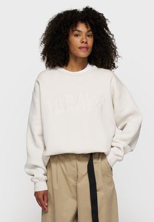 Felpa beige chiaro con lettering in rilievo "10DAYS", maniche larghe e una vestibilità rilassata. Abbinata a pantaloni chiari.