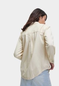 Lichtbeige lange mouwen shirt met een zachte textuur, knoopsluiting op de manchetten, een gebogen zoom en een geplooid achterontwerp.