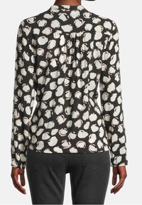 Camicia a maniche lunghe con sfondo nero e motivi astratti in crema e rosa pallido. Il retro presenta dettagli a pieghe e un collo arrotondato.