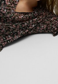 Blusa negra con estampado floral que presenta pequeñas flores rosas y azules, tejido ligero, corte holgado, con una textura suave y fluida.