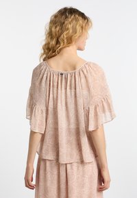 Blusa rosa pallido con vestibilità morbida, delicati maniche a volant e un tessuto leggero e morbido con un sottile motivo decorativo.