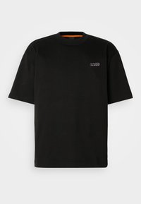 T-shirt noir à manches courtes et col rond avec un petit logo "BOSS" sur la poitrine gauche, sur un fond clair uni.