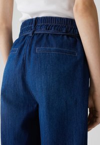 Dunkelblaue Jeanshose mit elastischem Bund, verfügt über eine glatte Textur, zwei Gesäßtaschen und einen geraden Schnitt.