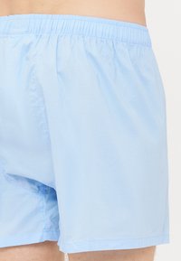 Helle blaue Baumwoll-Badehosen mit einem elastischen Bund, die ein einfaches Design und subtile Nahtdetails aufweisen, gefertigt für Komfort.