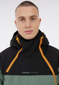 Giacca a vento nera e verde con cappuccio regolabile, zip arancioni e logo sul petto con la scritta "PROTEST PVRE GREEN." Tessuto dalla consistenza liscia.