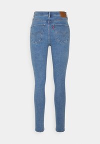Jeans delgados de mezclilla azul con una cintura de altura media, que cuentan con bolsillos traseros con detalles de costura y una etiqueta de cuero marrón en la cinturilla.
