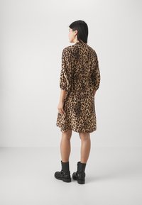 Robe léopard avec une taille ajustée, des manches trois-quarts et un ourlet évasé, associée à des bottines noires. Texture lisse.