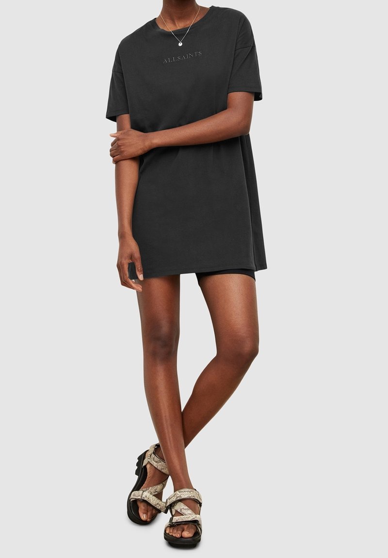 Robe t-shirt noire avec une coupe décontractée, des manches courtes et un logo "ALLSAINTS" en relief. Associée à des sandales texturées.