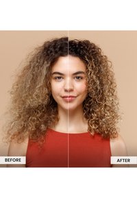 Femme aux cheveux bouclés portant un top sans manches rouge ; le côté gauche est frisé et moins défini, tandis que le côté droit présente des boucles lisses, brillantes et bien définies.