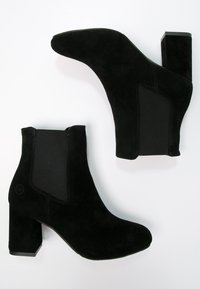 Bottes noires en suède à hauteur de cheville avec un bout pointu, des panneaux latéraux élastiques et un talon carré. Texture lisse avec un minimum de détails.