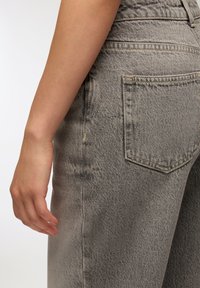 Szare dżinsy o średnim stanie, z klasyczną tylną kieszenią i gładką, lekko postrzępioną fakturą.